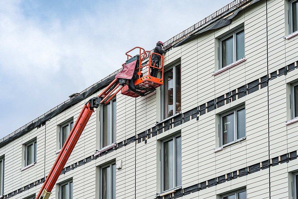 Hausansicht mit neuer Fassade und Arbeiter auf dem Kran