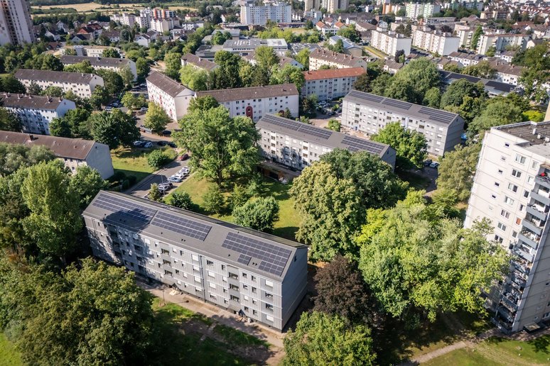 Blick von oben auf ein Wohngebiet mit vielen unterschiedlichen Mehrfamilienhäusern, dazwischen Rasenflächen und Laubbäume