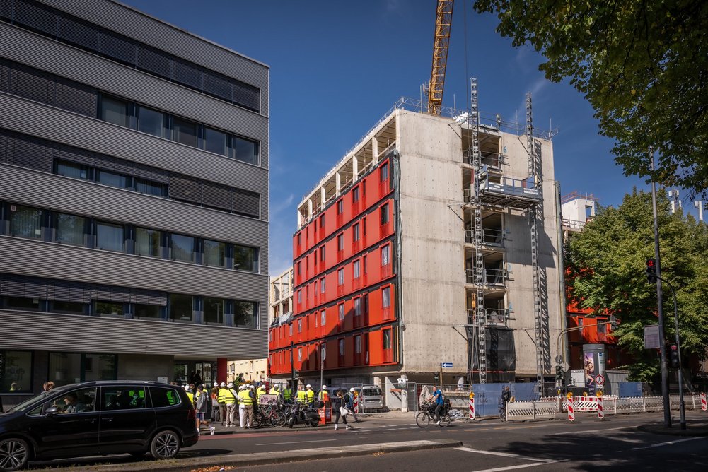 Gebäude während Sanierung mit bereits teilweise montierten roten, vorgefertigten Fassadenelementen