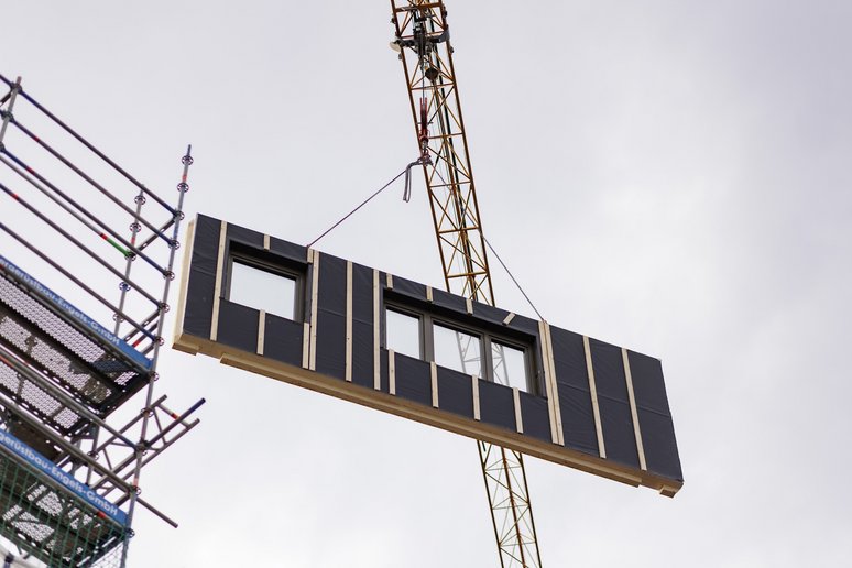Hausfassadenelement mit Fenstern schwebt an Kran.