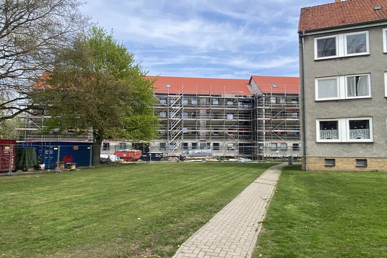 Fußweg mit Rasenflächen links und rechts, der zu Mehrfamilienhäusern führt.