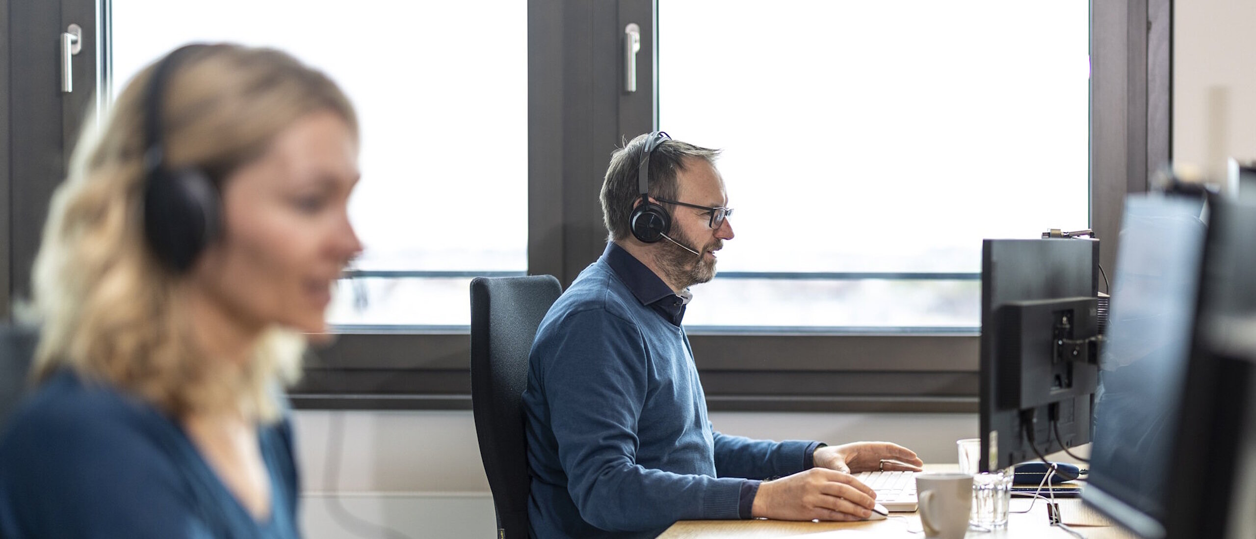 Zwei Personen mit Kopfhörer sitzen am Arbeitstisch und schauen auf Bildschirme.