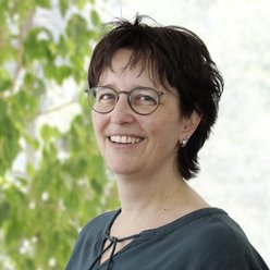 Person mit kurzen dunklen Haaren und Brille, Blusenshirt