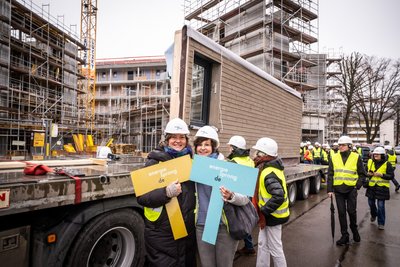 Bild zeigt: Zwei Frauen mit Bauhelmen halten jeweils ein Energiesprong-Schild in die Höhe auf einer Baustelle