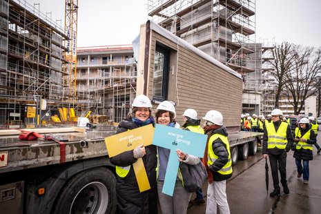 Bild zeigt: Zwei Frauen mit Bauhelmen halten jeweils ein Energiesprong-Schild in die Höhe auf einer Baustelle