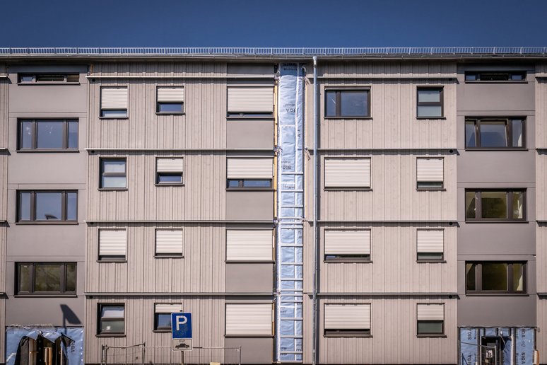 Blick auf die Fassade eines Mehrfamilinehauses mit Fenstern, Eingangsbereiche und Außenstrang für Gebäudetechnik noch nicht fertiggestellt