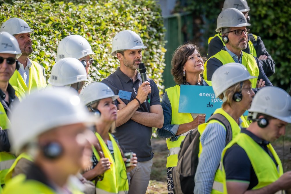 Personengruppe mit gelben Sicherheitswesten und weißen Bauhelmen auf den Köpfen