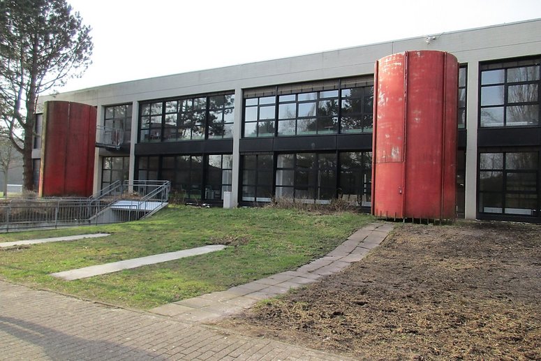 Schulgebäude zweigeschossig mit Flachdach unsaniert, davor stehen zwei große rote Tanks.