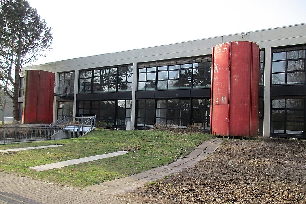 Schulgebäude zweigeschossig mit Flachdach unsaniert, davor stehen zwei große rote Tanks.