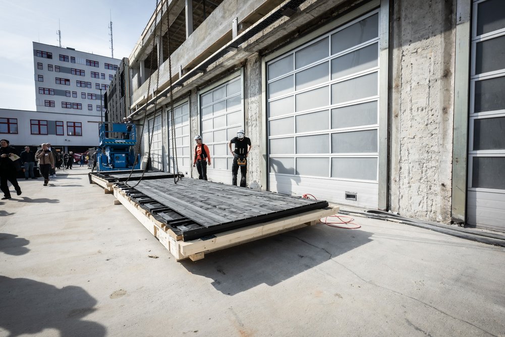 Die Feuerwache erhält eine neue Gebäudehülle aus 86 bis zu 8,58 Meter hohen und 2,36 Meter breiten Fassadenelementen. Fassadenelement liegt am Boden vor einem Gebäude.