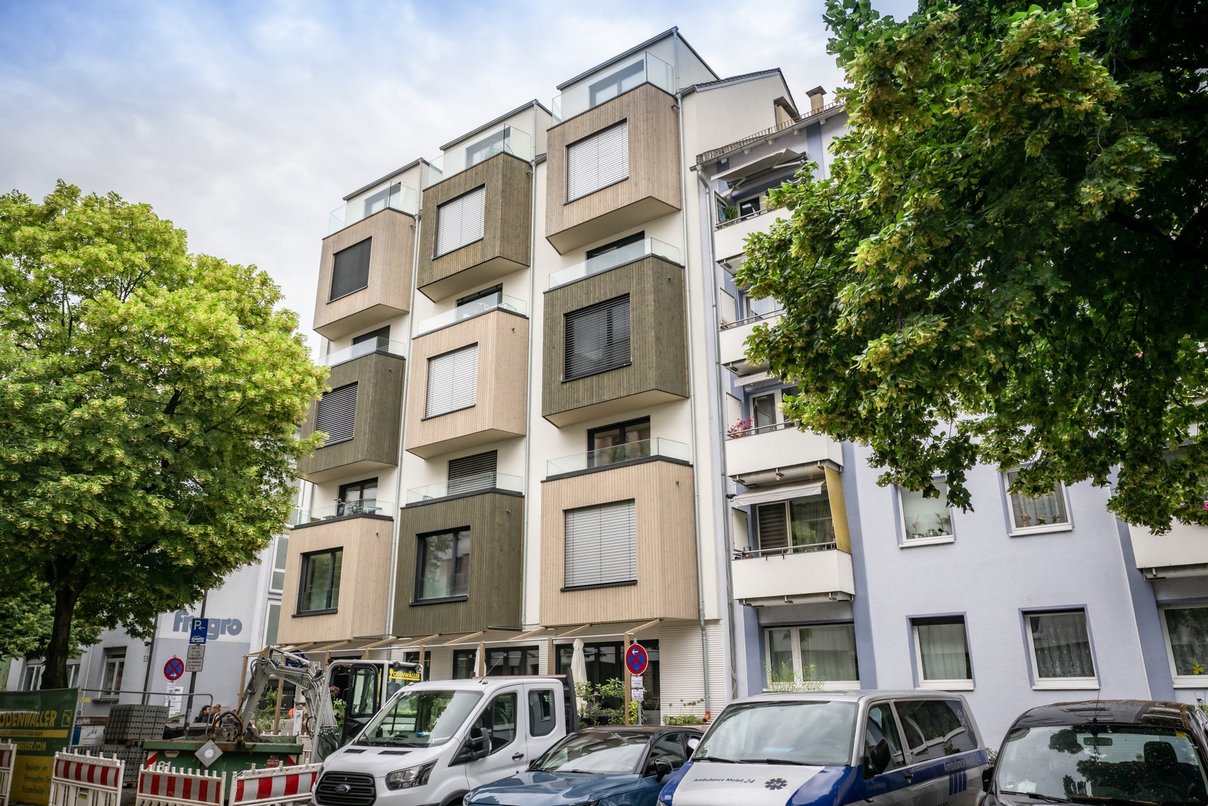 Mehrfamilienhaus, davor parkende Autos und zwei Laubbäume
