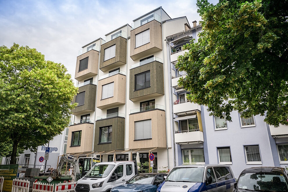 Mehrfamilienhaus, davor parkende Autos und zwei Laubbäume