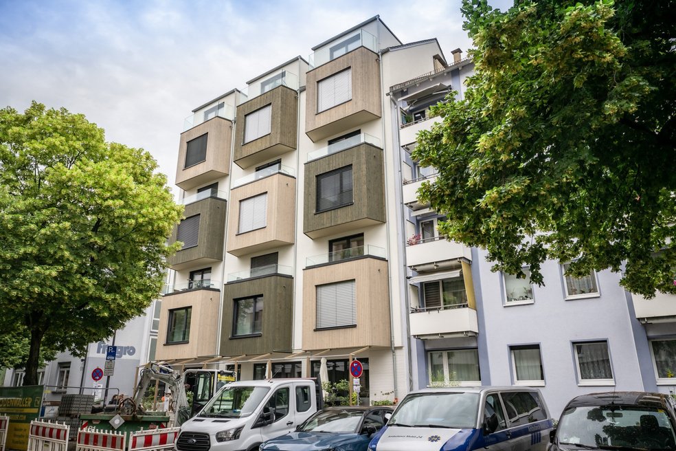 Mehrfamilienhaus, davor parkende Autos und zwei Laubbäume