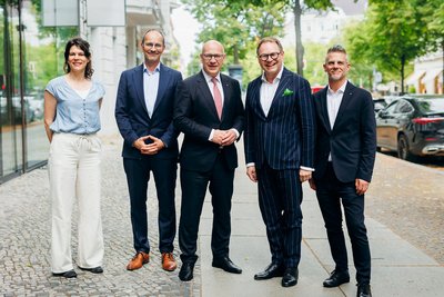 Fünf Personen stehen nebeneinander auf einem Fußweg für ein Gruppenbild.