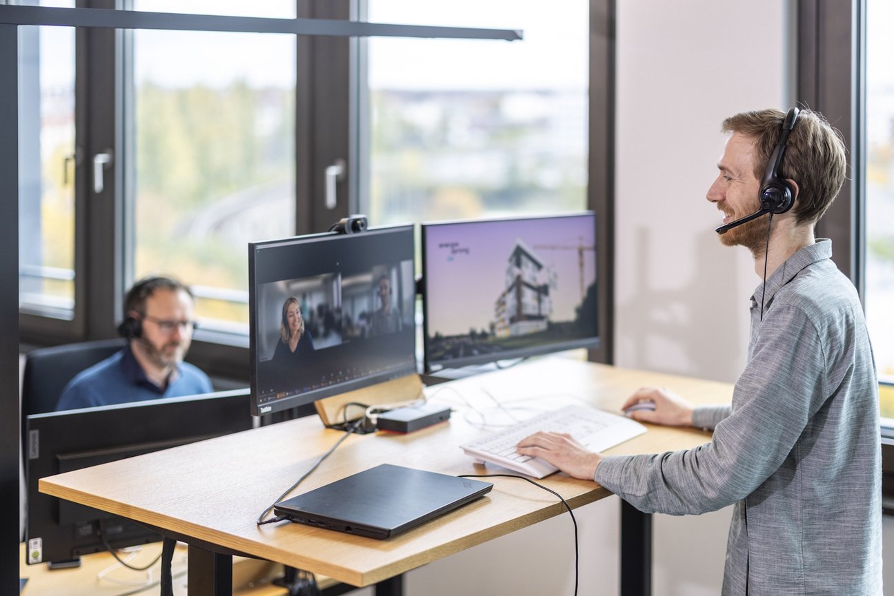 Zwei Personen mit Headset am Arbeitsplatz mit Monitoren in einem Büro
