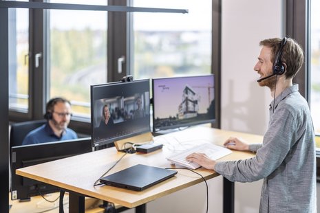 Zwei Personen mit Headset am Arbeitsplatz mit Monitoren in einem Büro