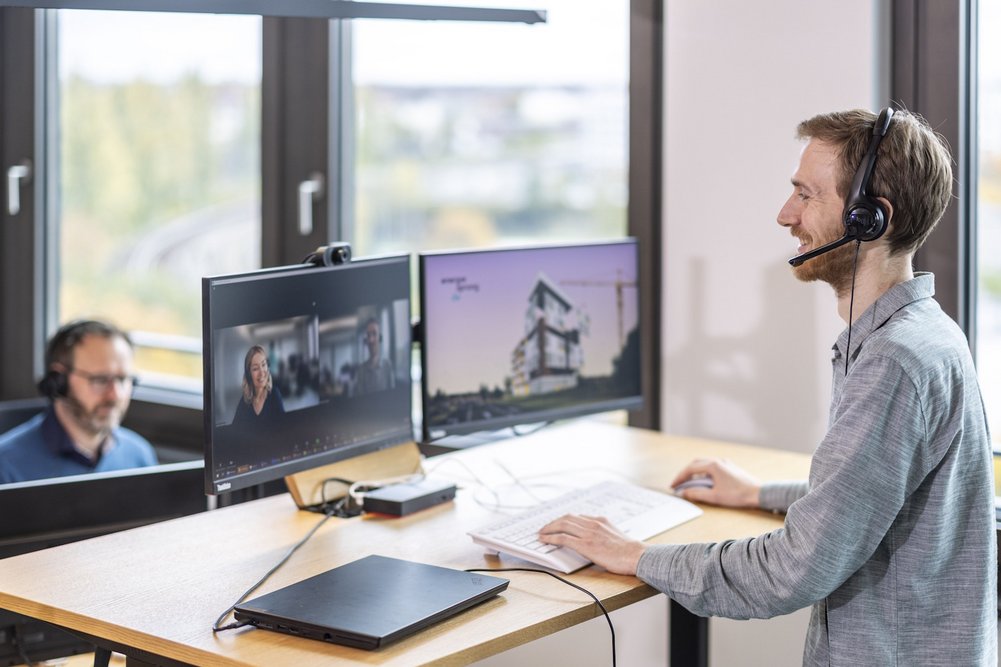 Zwei Personen mit Headset am Arbeitsplatz mit Monitoren in einem Büro