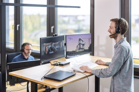 Zwei Personen mit Headset am Arbeitsplatz mit Monitoren in einem Büro