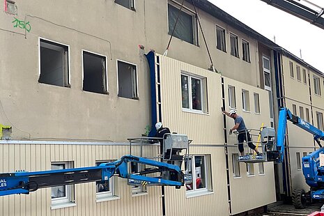Kran mit Arbeitern an Gebäude mit teilweise neuer Fassade