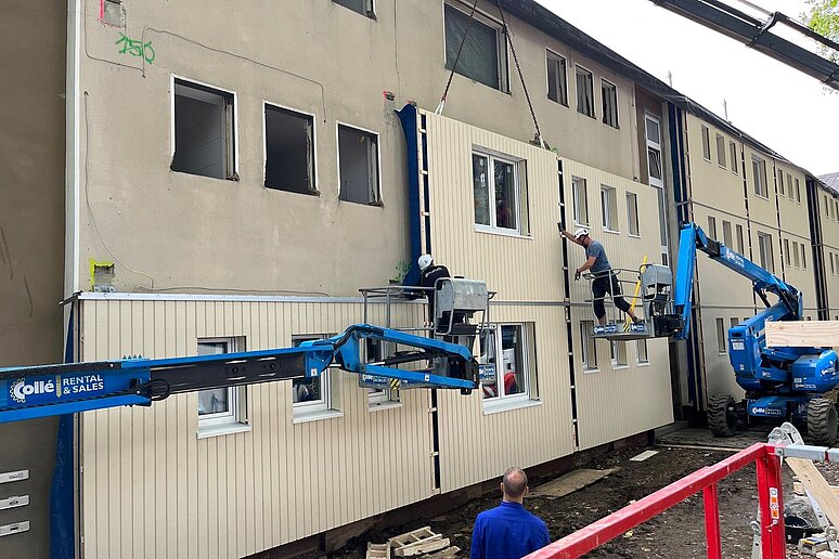 Kran mit Arbeitern an Gebäude mit teilweise neuer Fassade