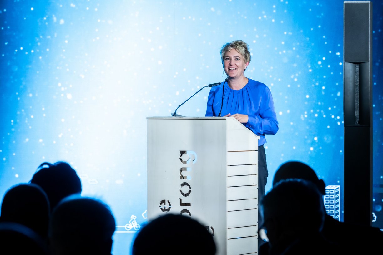 Weibliche Person steht hinter einem Rednerpult und schaut zum Publikum davor.