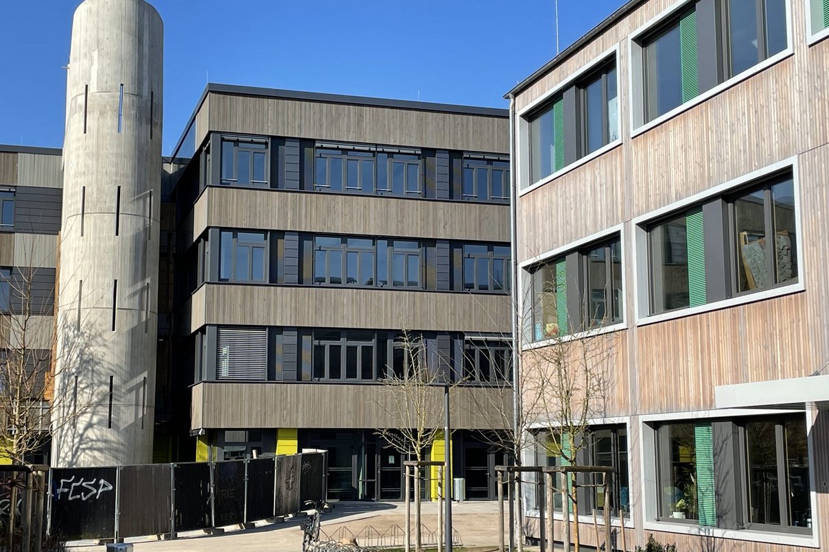 Gebäude auf einem Campus-Gelände, im Hintergrund blauer wolkenloser Himmel
