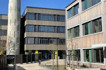 Gebäude auf einem Campus-Gelände, im Hintergrund blauer wolkenloser Himmel
