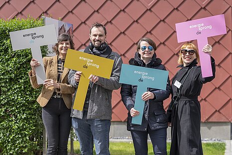 Vier personen stehen nebeneinander mit je einem farbigen Schild in der Hand mit dem Aufdruck "energiesprong.de".