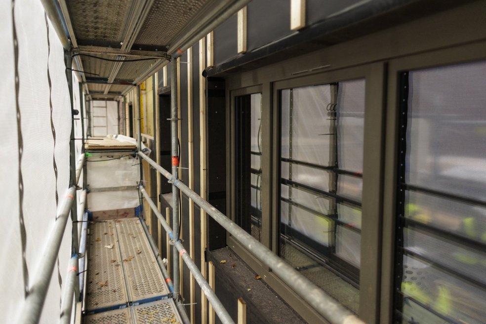 Gang auf einem Baugerüst zwischen Fensterfront des Gebäudes und Schutzplane