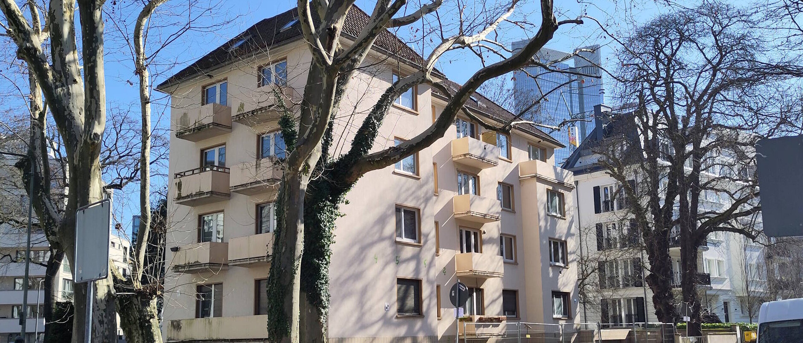 Mehrfamilienhaus viergeschossig mit kleinen Balkonen, unsaniert. Davor eine Straße mit Bäumen ohne Blätter.