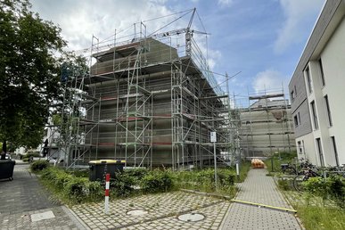 Blick auf mehrere Mehrfamilienhäuser, die teils saniert werden und Baugerüst haben, Fußweg durch die Wohnanlage