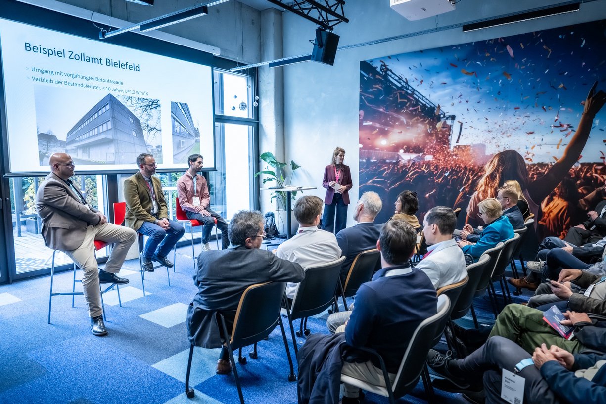 Personen sitzen in einem Veranstaltungsraum während einer Präsentation.