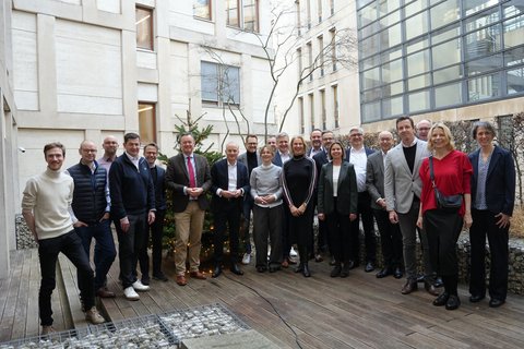 Personen stehen nebeneinander und posieren für das Gruppenbild, im Hintergrund ein modernes Gebäde. 