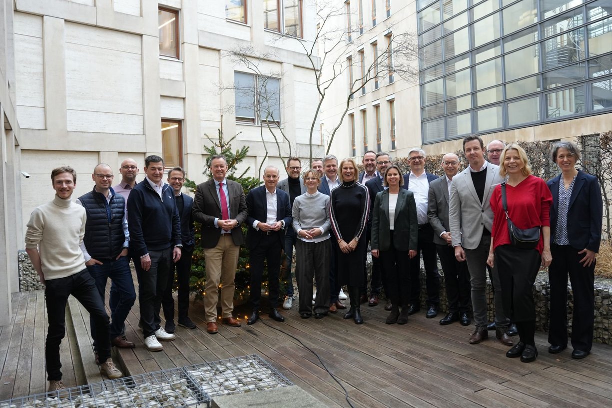 Personen stehen nebeneinander und posieren für das Gruppenbild, im Hintergrund ein modernes Gebäde. 