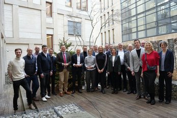 Personen stehen nebeneinander und posieren für das Gruppenbild, im Hintergrund ein modernes Gebäde. 