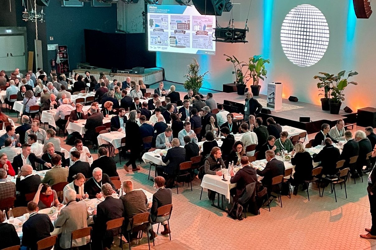 Viele Menschen an Tischen beim Essen in großer beleuchteter Halle