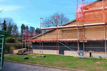 Außenansicht Turnhalle mit Schrägdach während Sanierung, davor Baugerüst und Grünflächen