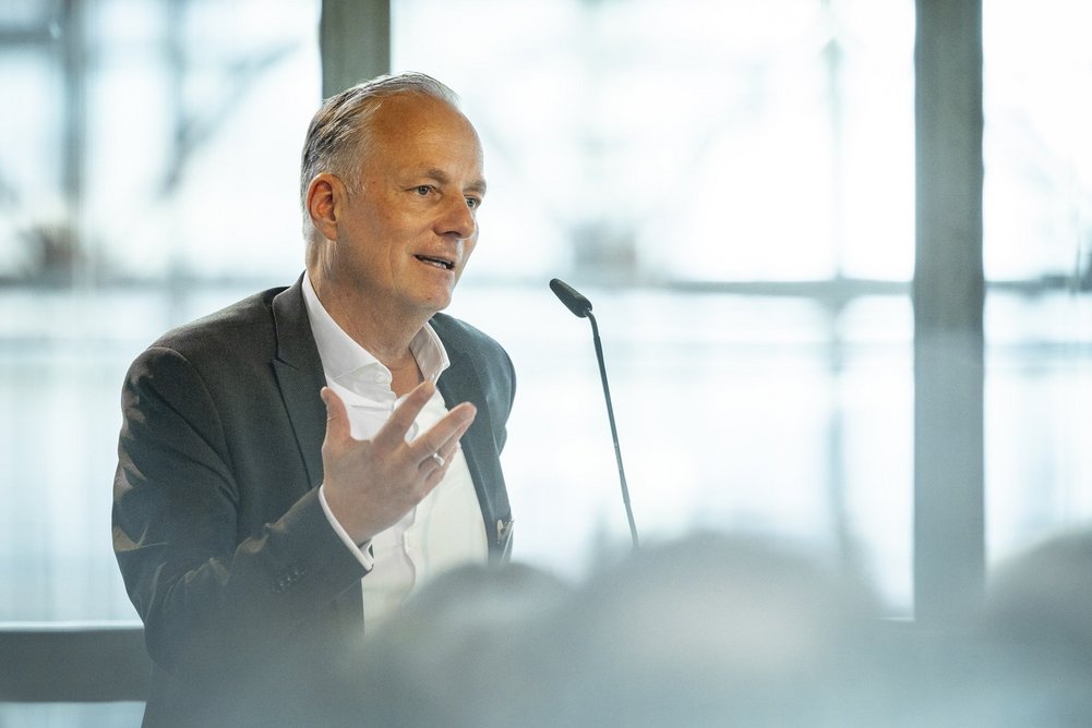 Alexander Rychter Person in Business-Kleidung spricht am Pult mit Mikrofon.