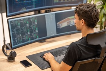 Bild zeigt: Mensch von hinten, der am PC sitzt und ein Gebäude plant mit einem Programm das ein 3D Modell eines Hauses zeigt