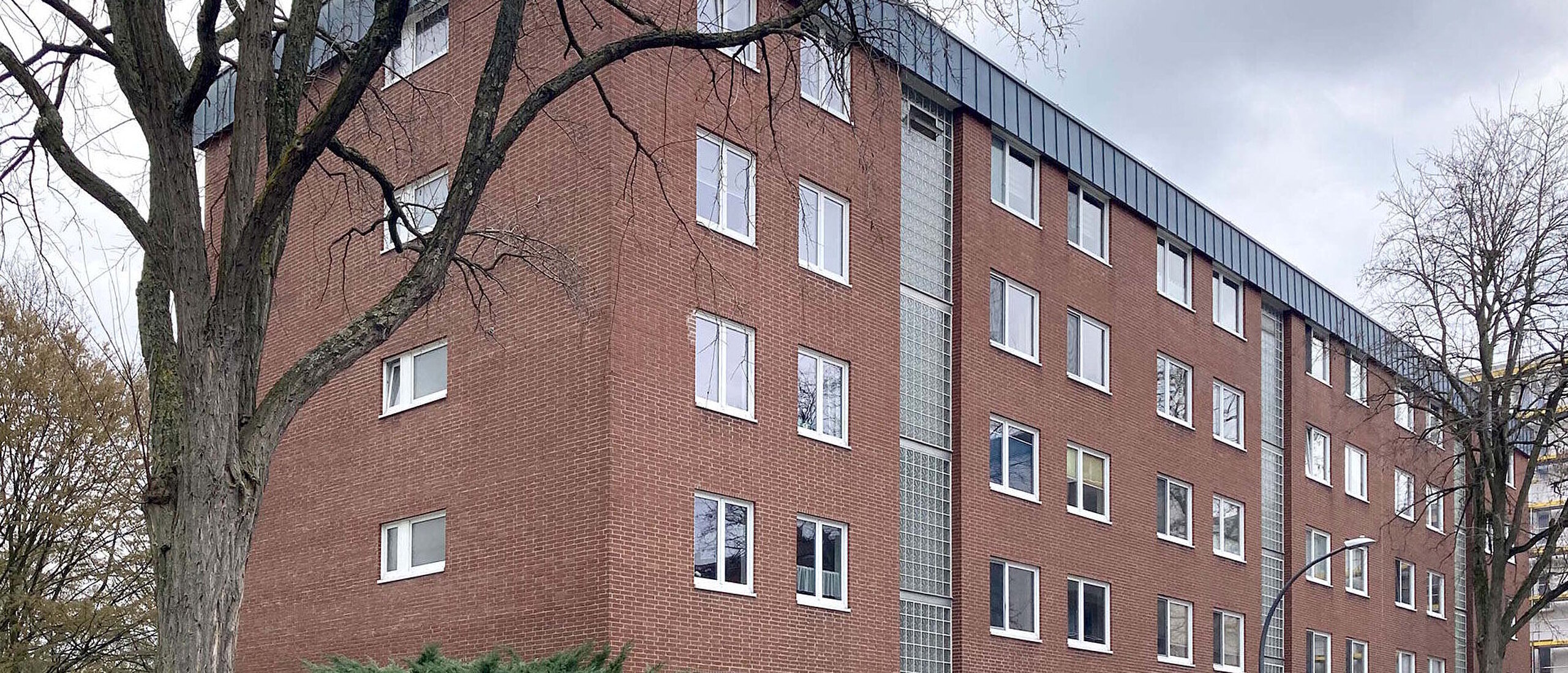 Mehrfamilienhaus fünfgeschossig, Klinkerfassade, davor parkende Autos und Bäume
