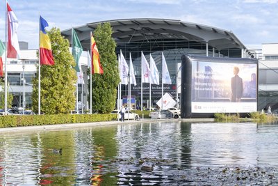 Messeglände in München. Gebäude aus Glasfasade. Viele Fahnen von Unternehmen und ein kleiner industrieller Deko-Teich.