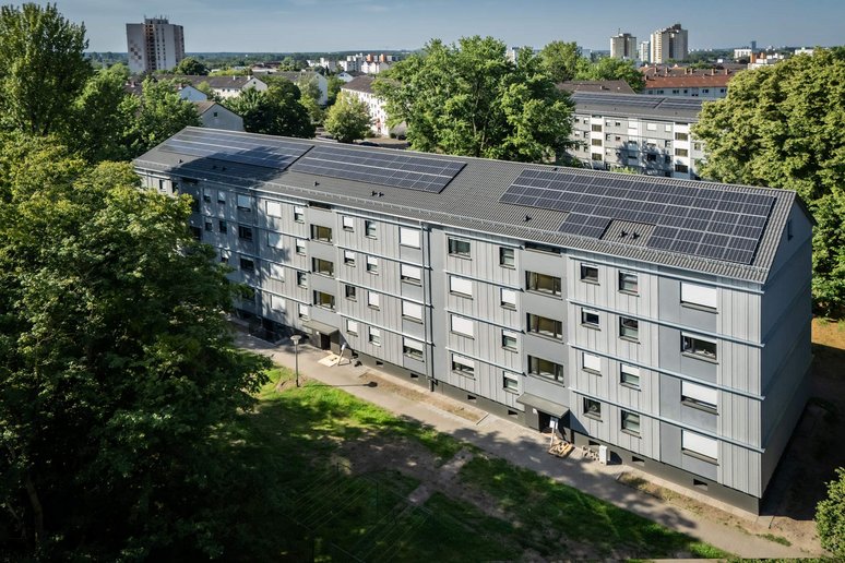 Blick von oben auf ein neu saniertes Mehrfamilienhaus viergeschossig, graue Fassade, Photovoltaikanlagen auf dem Schrägdach