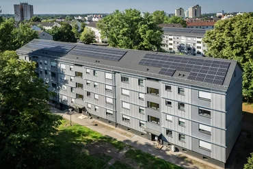 Blick von oben auf ein neu saniertes Mehrfamilienhaus viergeschossig, graue Fassade, Photovoltaikanlagen auf dem Schrägdach