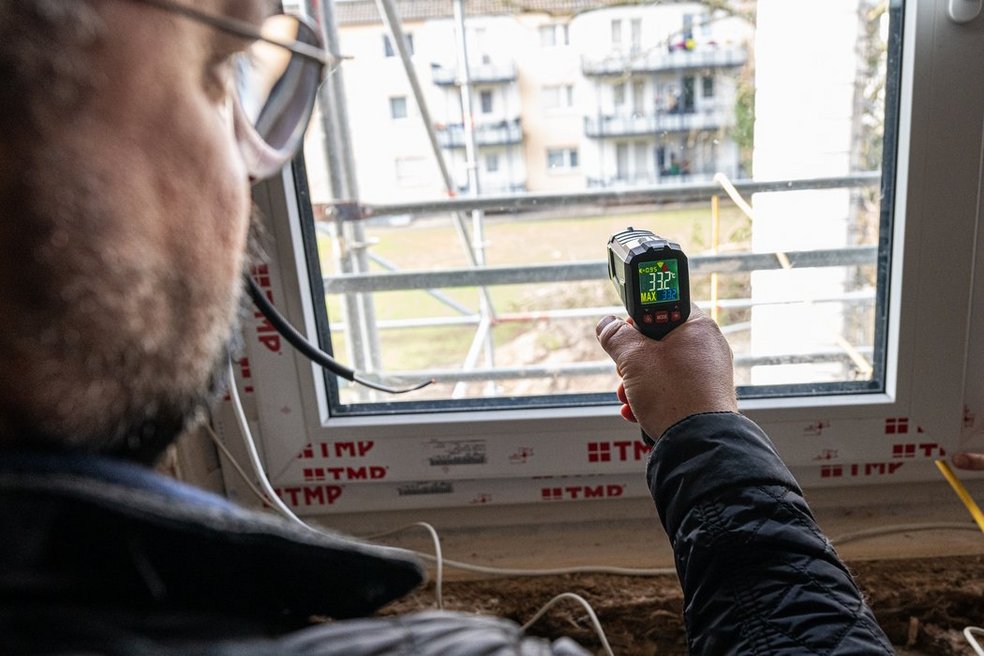 Person misst mit einem technischen Gerät die Temperatur an einem Fenster.