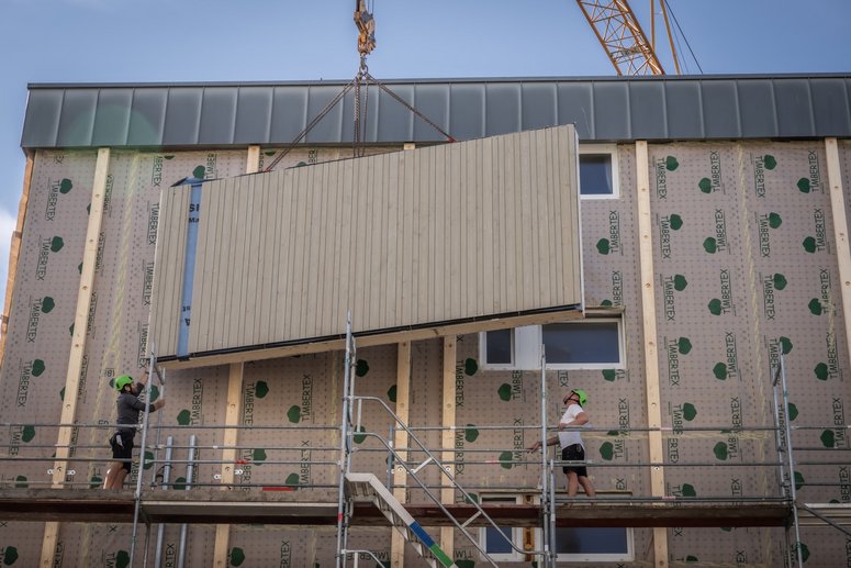 Wohngebäude während Sanierung, Bauarbeiter platzieren vorgefertigtes Fassadenelement zur Montage an der Fassade