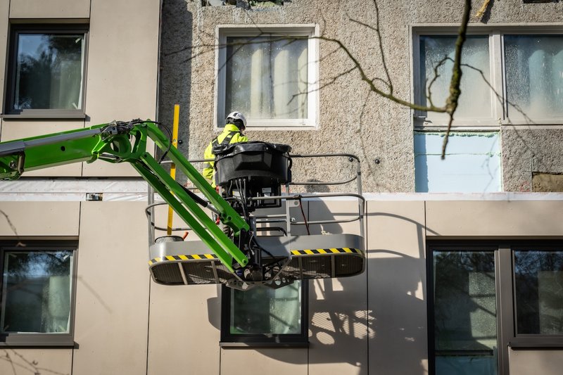 Bauarbeiter im Steiger montiert Fassadenelement an ein Plattenbaugebäudes.