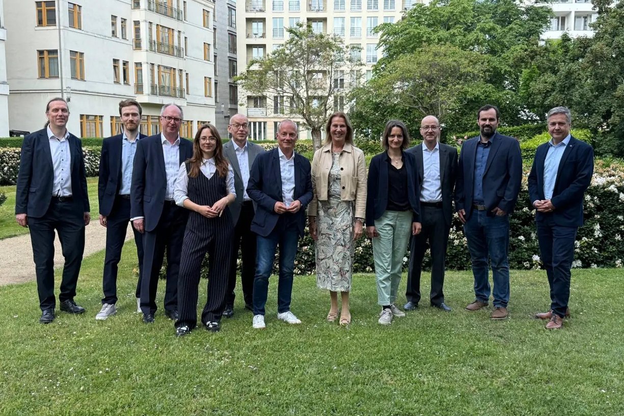 Der Begleitkreis zur Projektgruppe bei seinem Treffen in Berlin Elf Personen in Business-Kleidung stehen nebeneinander auf dem Rasen für ein Gruppenbild, im Hintergrund mehrgeschossige Gebäude