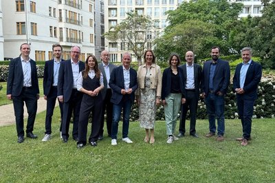 Elf Personen in Business-Kleidung stehen nebeneinander auf dem Rasen für ein Gruppenbild, im Hintergrund mehrgeschossige Gebäude