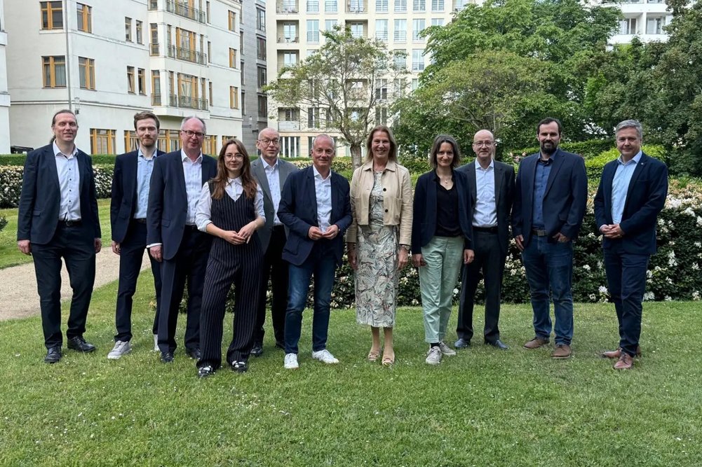 Der Begleitkreis zur Projektgruppe bei seinem Treffen in Berlin Elf Personen in Business-Kleidung stehen nebeneinander auf dem Rasen für ein Gruppenbild, im Hintergrund mehrgeschossige Gebäude