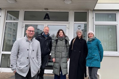 Fünf Personen in warmer Kleidung stehen nebeneinander vor einem Gebäudeeingang. 